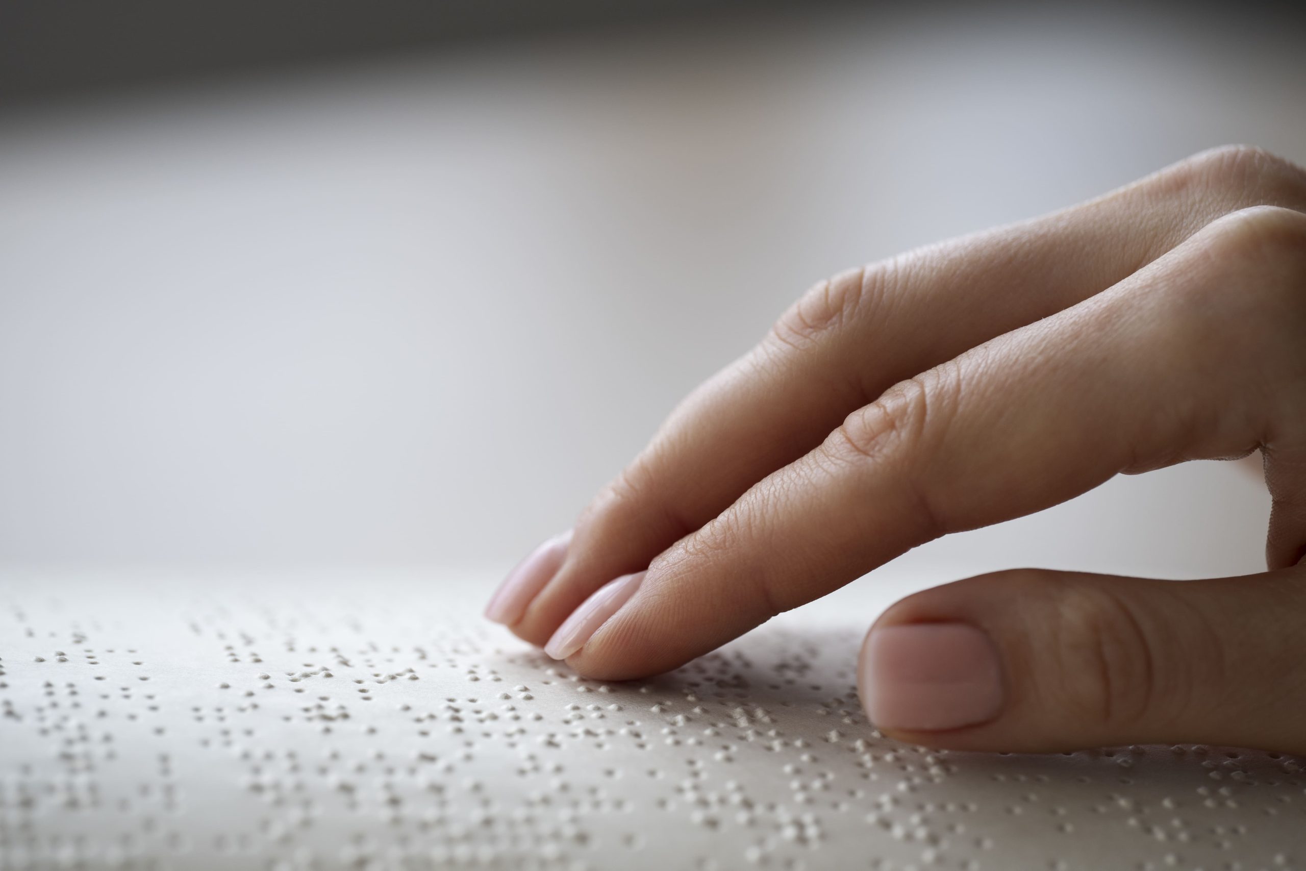 Mão de uma pessoa tocando sobre o livro escrito em braille.